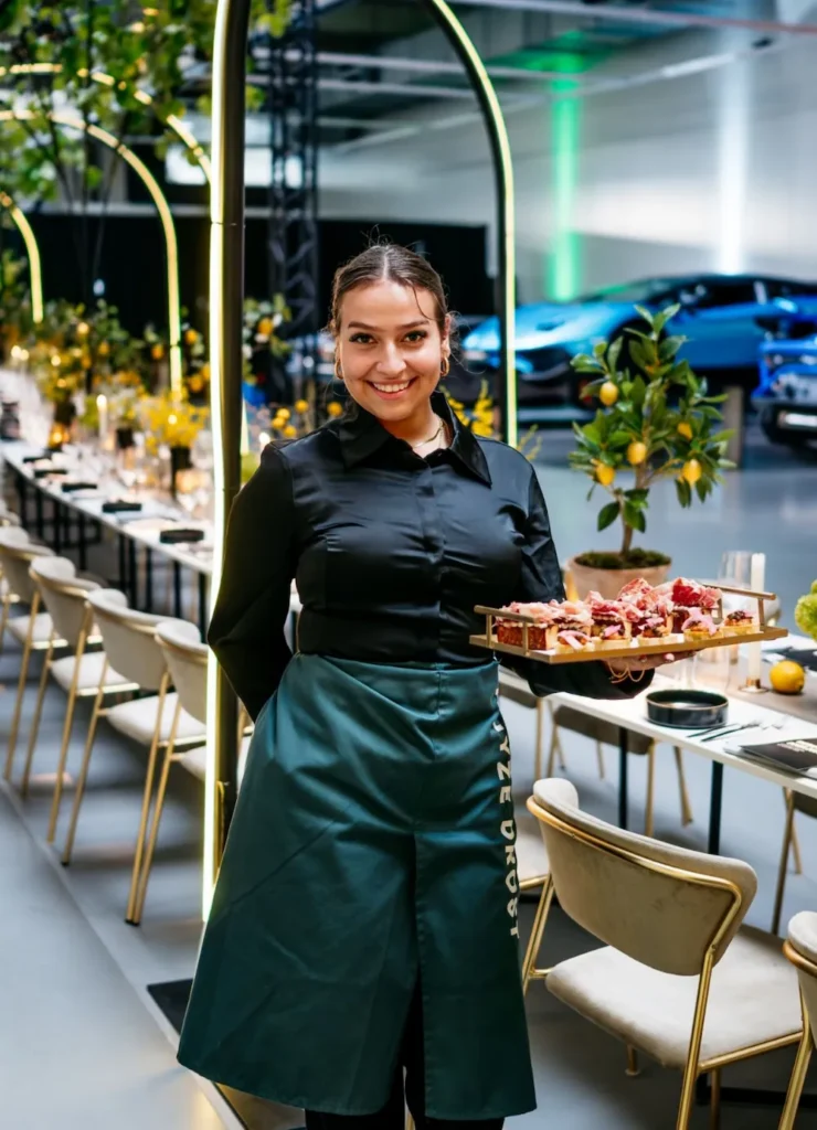 Bediening loopt glimlachend met een schaal hapjes door een stijlvol gedekte dinerlocatie.