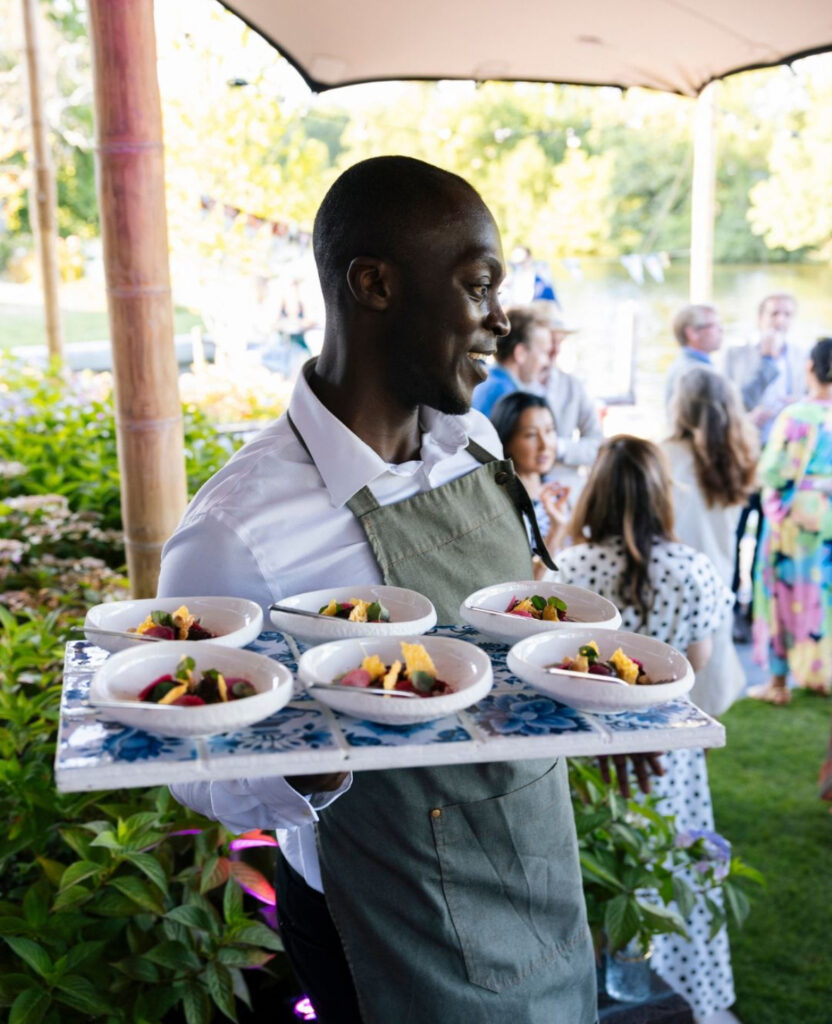Gastheer van Served With Passion serveert fine-dining gerechten tijdens een high-end buitenevent in samenwerking met Sonah Fine Foods. De foto straalt gastvrijheid, kwaliteit en verfijnde service uit, met een ontspannen sfeer vol zomerse luxe.