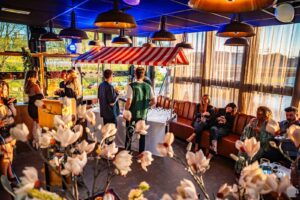 Mensen genieten van drankjes en gesprekken in een sfeervol ingerichte ruimte met een bar onder een rood-wit gestreept dakje.