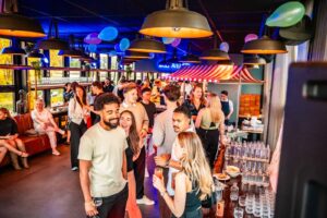 Mensen genieten van een feestelijke borrel in een kleurrijk versierde ruimte met drankjes en gezelligheid.