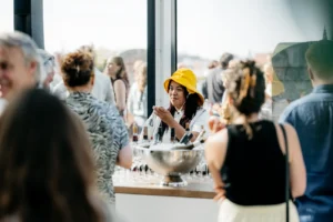 Vrouw met gele hoed schenkt drankjes in op een drukbezocht evenement bij een buitenbar.