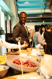 Man in pak lacht terwijl hij bij een drukbezocht buffet met hapjes staat tijdens een evenement.