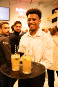 Een glimlachende ober serveert drankjes tijdens een drukbezocht evenement.