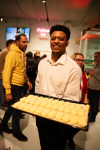 Man in witte blouse presenteert een dienblad met gele SWP-201 ijsjes op een drukbezocht evenement.