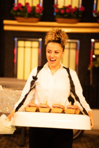 Vrouw in wit overhemd serveert miniburgers uit een draagtray op een evenement.