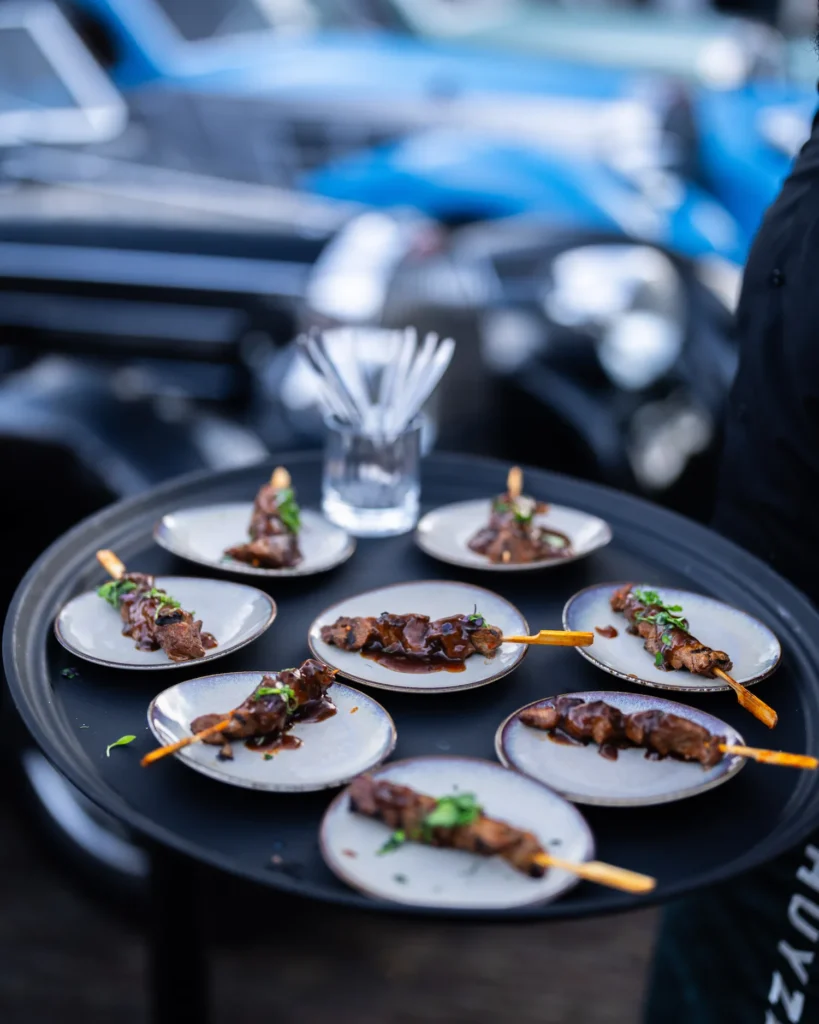 Ronde dienblad met smakelijke satéspiesjes op kleine bordjes, geserveerd tijdens The Perridon Collection event bij Wheels Marienwaerdt.