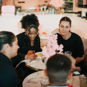 Vier mensen zitten rond een marmeren tafel en voeren een grondige selectiegesprek met formulieren en notities.