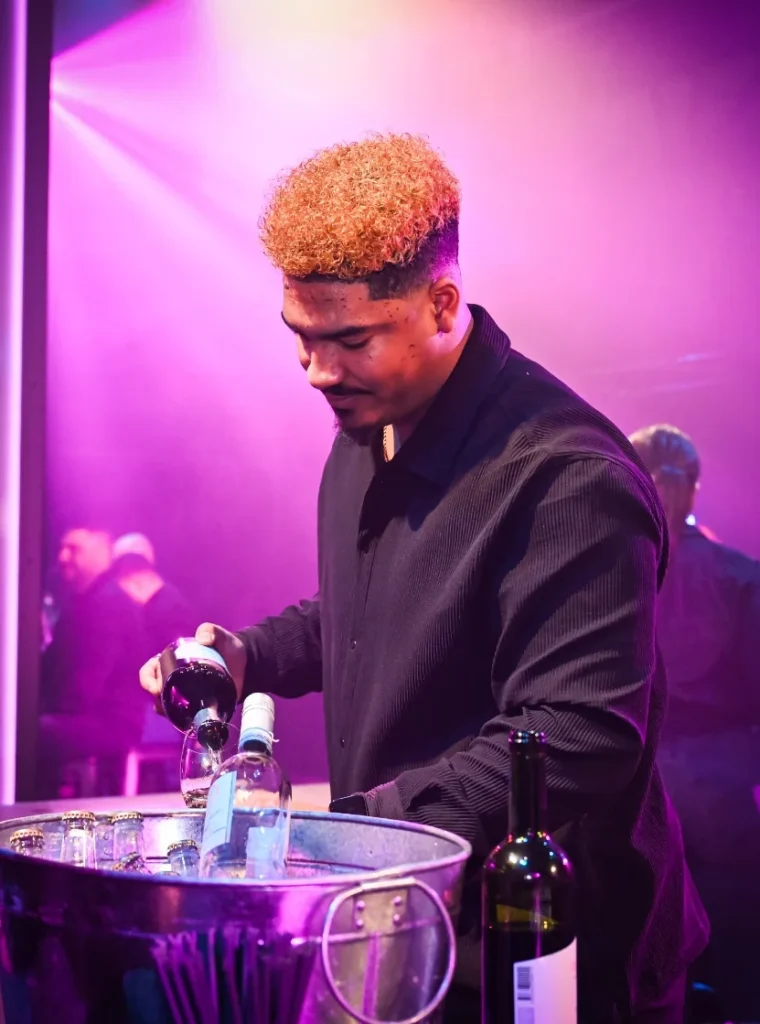 Barman schenkt rode wijn in een glas tijdens een evenement met paarse verlichting.