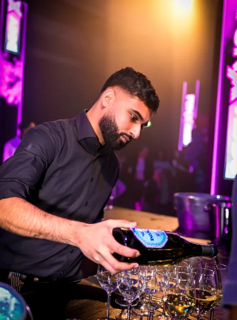 Barman van im-bartenders schenkt wijn in glazen tijdens een evenement met paarse verlichting.