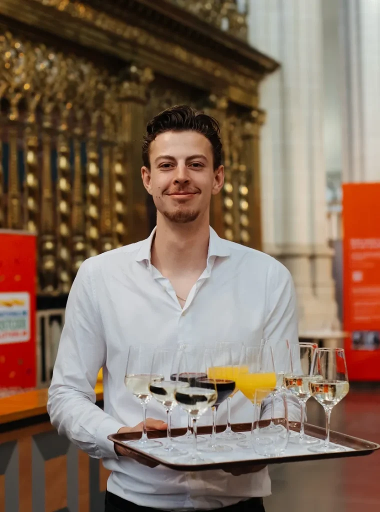 Ober met wit overhemd serveert drankjes op een dienblad in een chique, klassiek interieur.