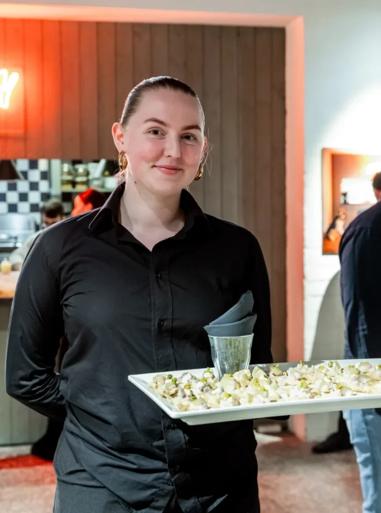 Vriendelijke serveerster in zwarte kleding serveert een schaal met hapjes tijdens een evenement.