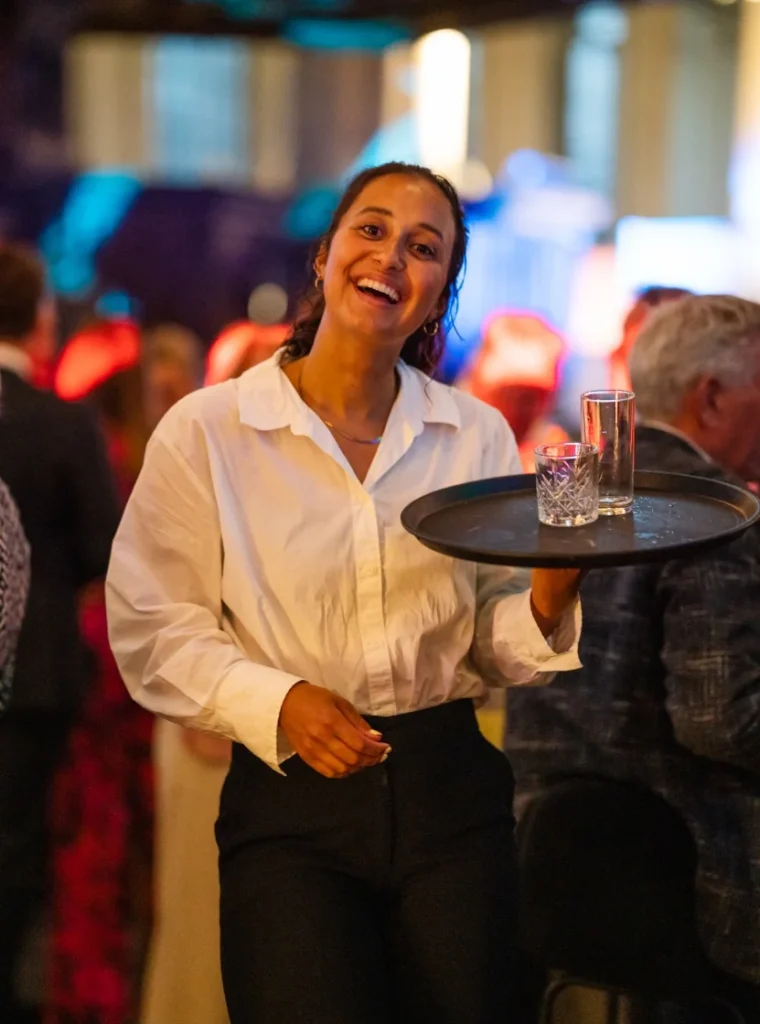 Vriendelijke serveerster met een dienblad met glazen tijdens een evenement.