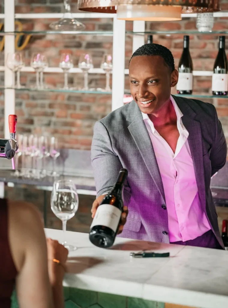 Man in pak overhandigt een fles wijn aan een klant aan de bar.
