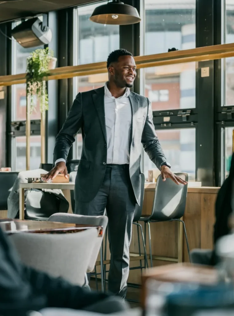 Zakelijke man in pak spreekt met een glimlach staand in een moderne vergaderruimte.