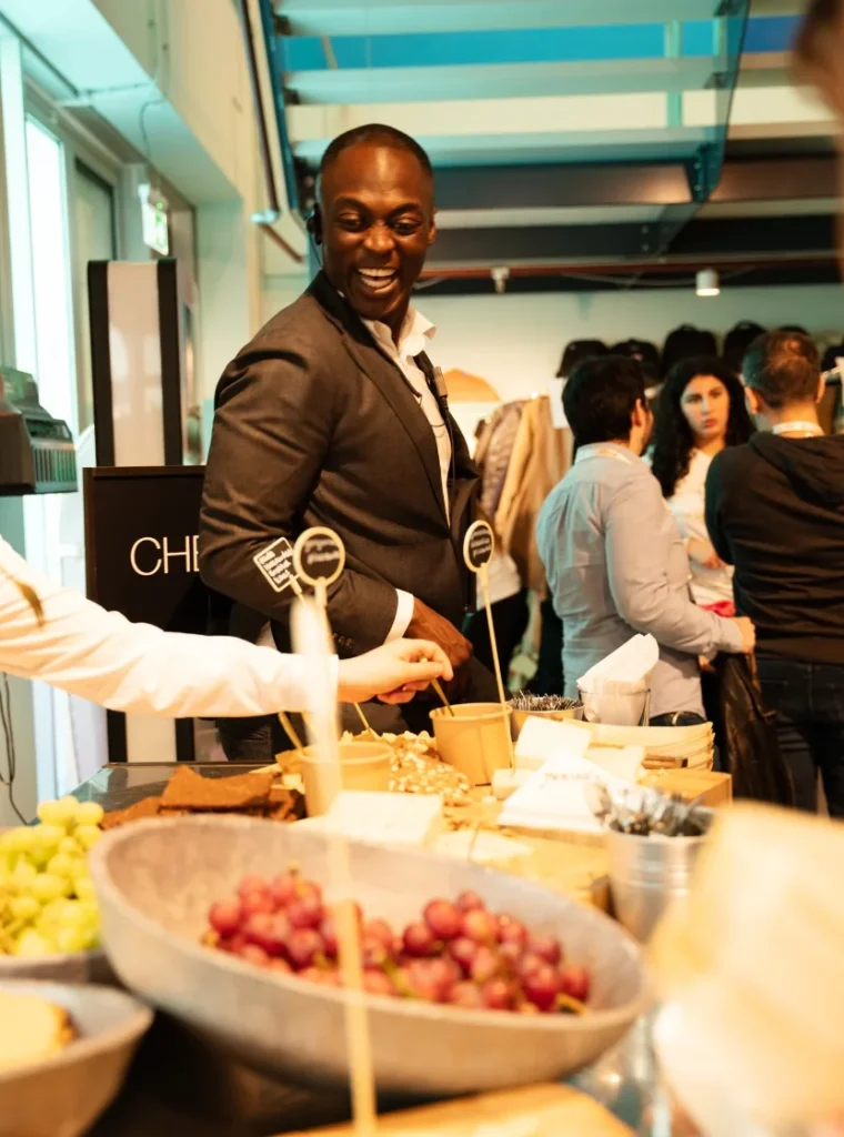 Man in pak lacht terwijl hij bij een buffet met hapjes staat tijdens een bijeenkomst.