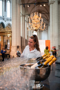 Vrouw schenkt champagne in glazen tijdens een evenement in een sfeervolle kerk met kroonluchter.