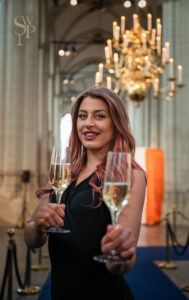 Vrouw in een elegante setting houdt twee glazen champagne vast terwijl ze glimlacht naar de camera.