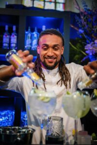 Barman maakt gin-tonics klaar met tonic water in een sfeervol verlichte bar.