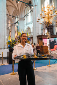 Vriendelijke serveerster met een dienblad vol hapjes in een sfeervol verlichte kerkruimte.