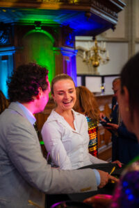 Twee mensen praten en lachen tijdens een feestelijke bijeenkomst met kleurrijke verlichting.