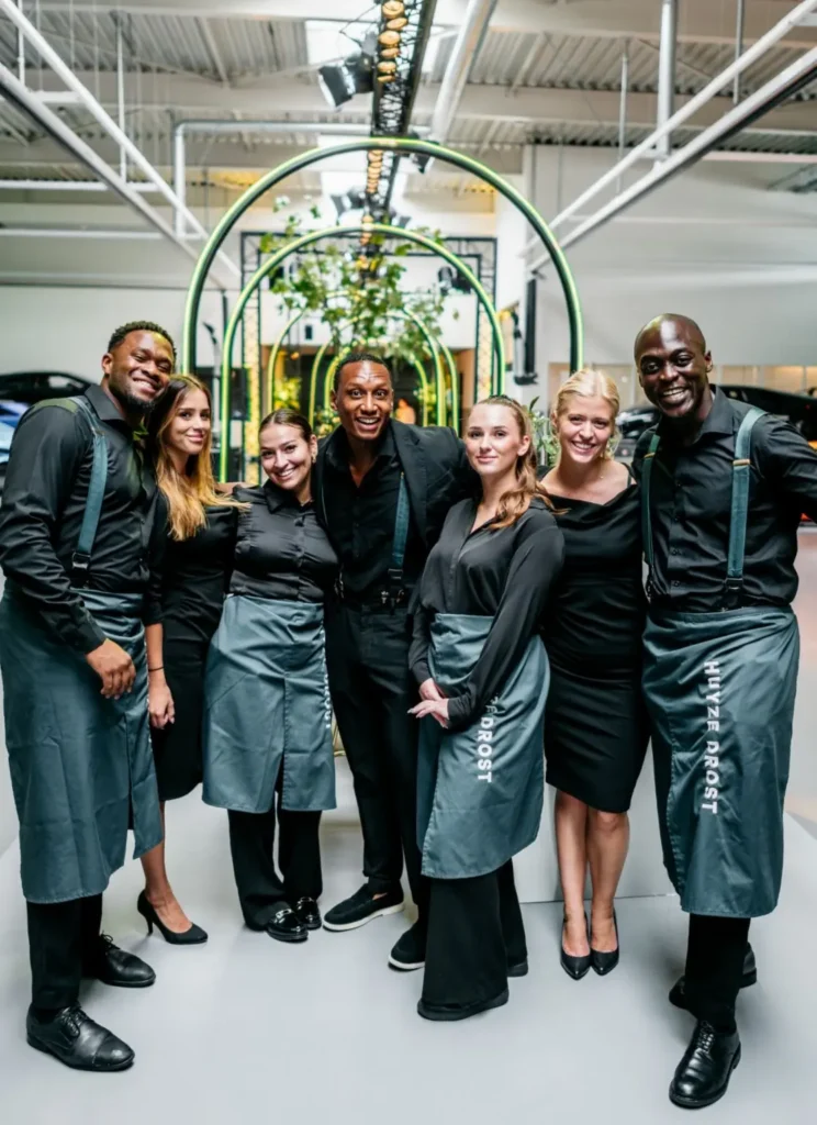 Groepsfoto van het team van Huize Drost in zwarte kleding en grijze schorten, lachend tijdens een evenement.